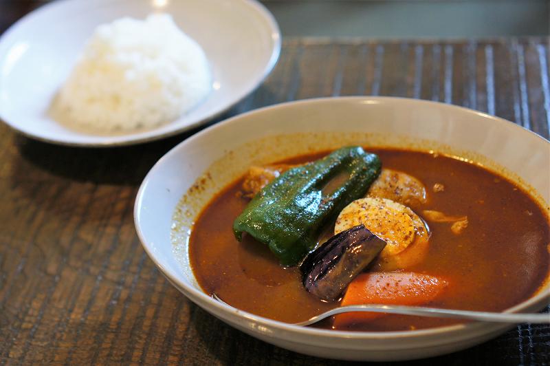 鶏肉と野菜、ゆで卵などが入ったスープカレーとごはんのお皿がテーブルに置かれいている