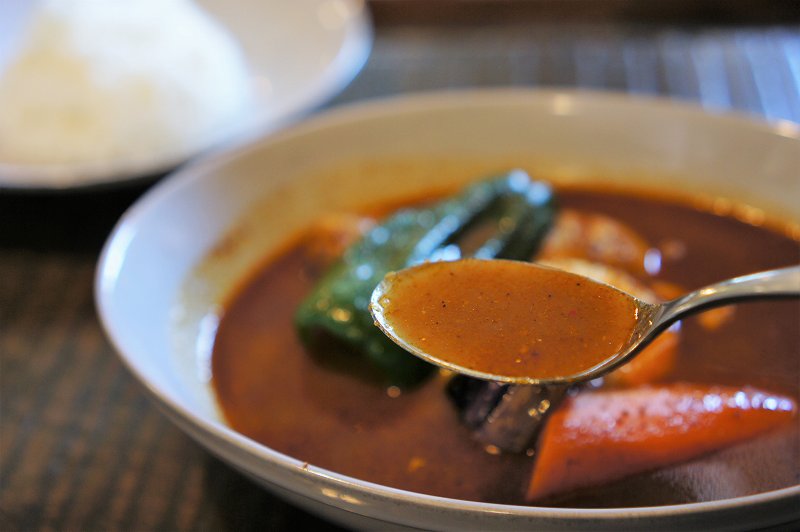 鶏肉と野菜、ゆで卵などが入ったスープカレーをスプーンですくった様子