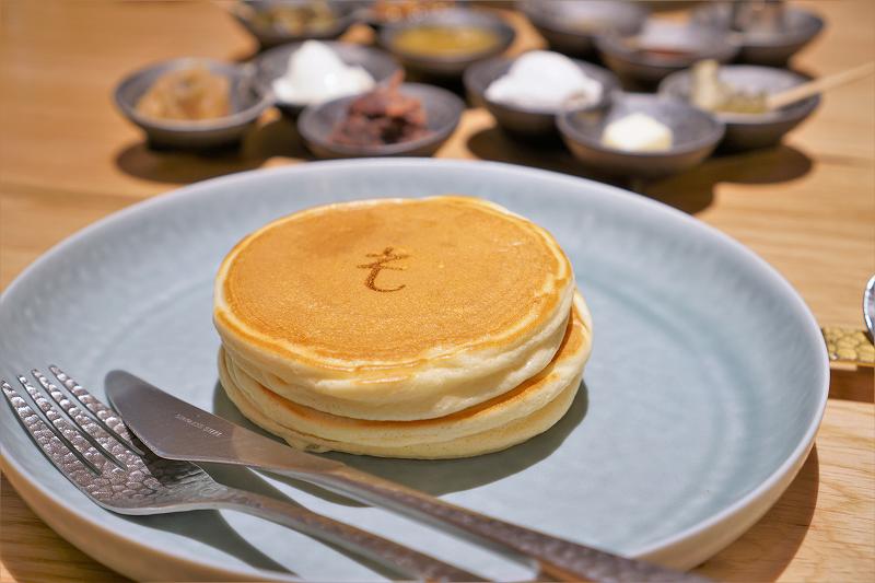 「も」の焼き印が入ったホットケーキとトッピングがテーブルに置かれている