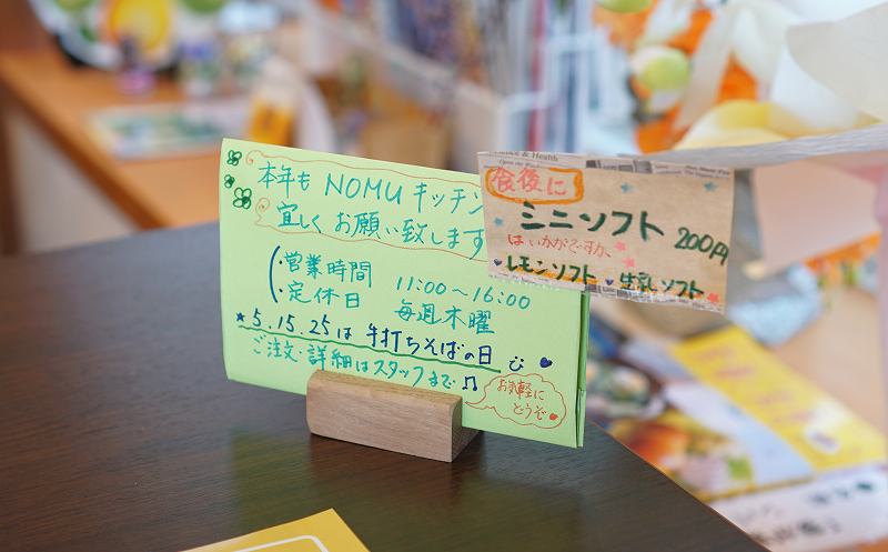 NOMUキッチンの営業時間、定休日、手打ちそばの日の案内がテーブルに置かれている