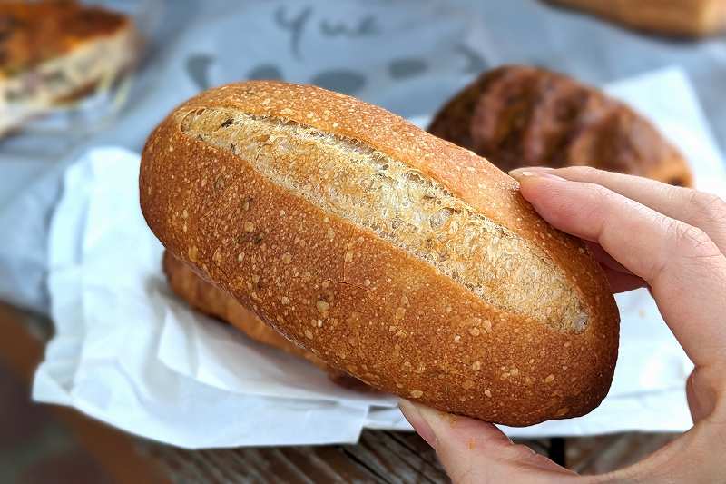 札幌「boulangerie yue.（ブーランジェリーユエ）」のクミンフランスパンを手に持っている様子